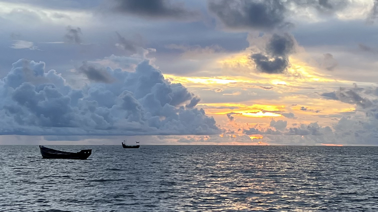 Sunset over the sea with bright clouds and two fishing boats